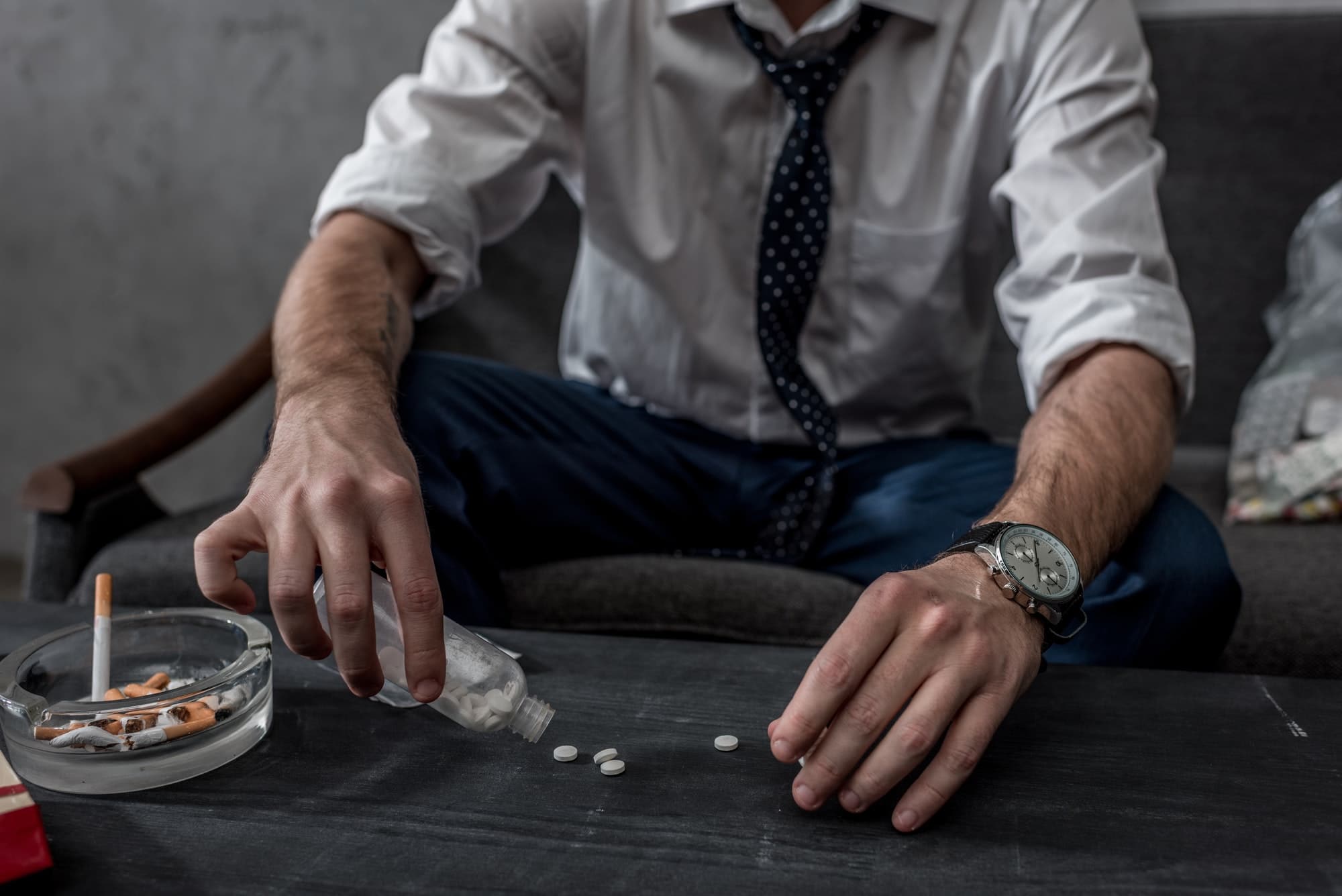businessman with drug addiction pouring pills on table from bottle